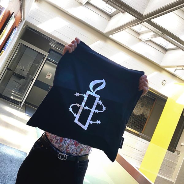 Ihminen pitelee käsiensä välissä mustaa kangaskassia, jossa on Amnestyn kynttilälogo.