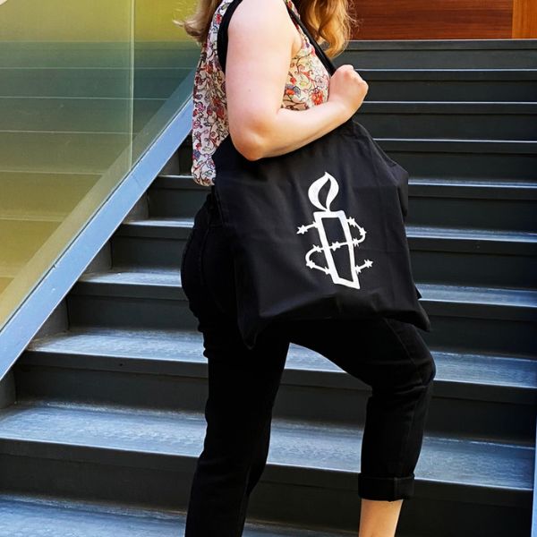 Portailla seisova ihminen pitelee mustaa kangaskassia, jossa on Amnestyn kynttilälogo.