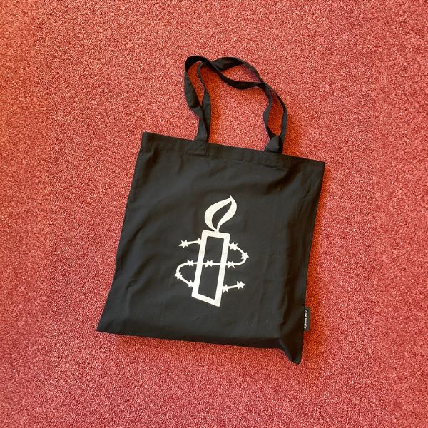 Musta kangaskassi punaisella taustalla. Kassissa on Amnestyn kynttilälogo.