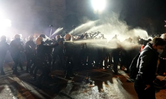 Poliisit seisovat rivissä ja sumuttavat kyynelkaasua tai pippurisumutetta mielenosoittajia päin