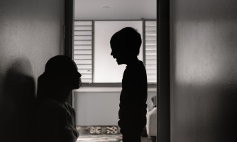 Vastavalokuva lapsesta, joka huutaa suu ammollaan ja hänen vieressään lattialla istuvasta vanhemmasta.