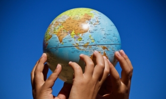 Maapallo pienoiskoossa, jota kannattelevat useat pienet kädet.