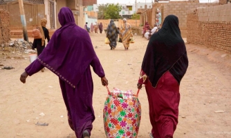 Kaksi ihmistä kävelee kauemmas kamerasta. He kantavat yhdessä isoa kassia.