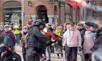 Väkijoukkoa torilla. Etualalla raskaisiin varusteisiin pukeutunut poliisi nostaa oranssia asetta.